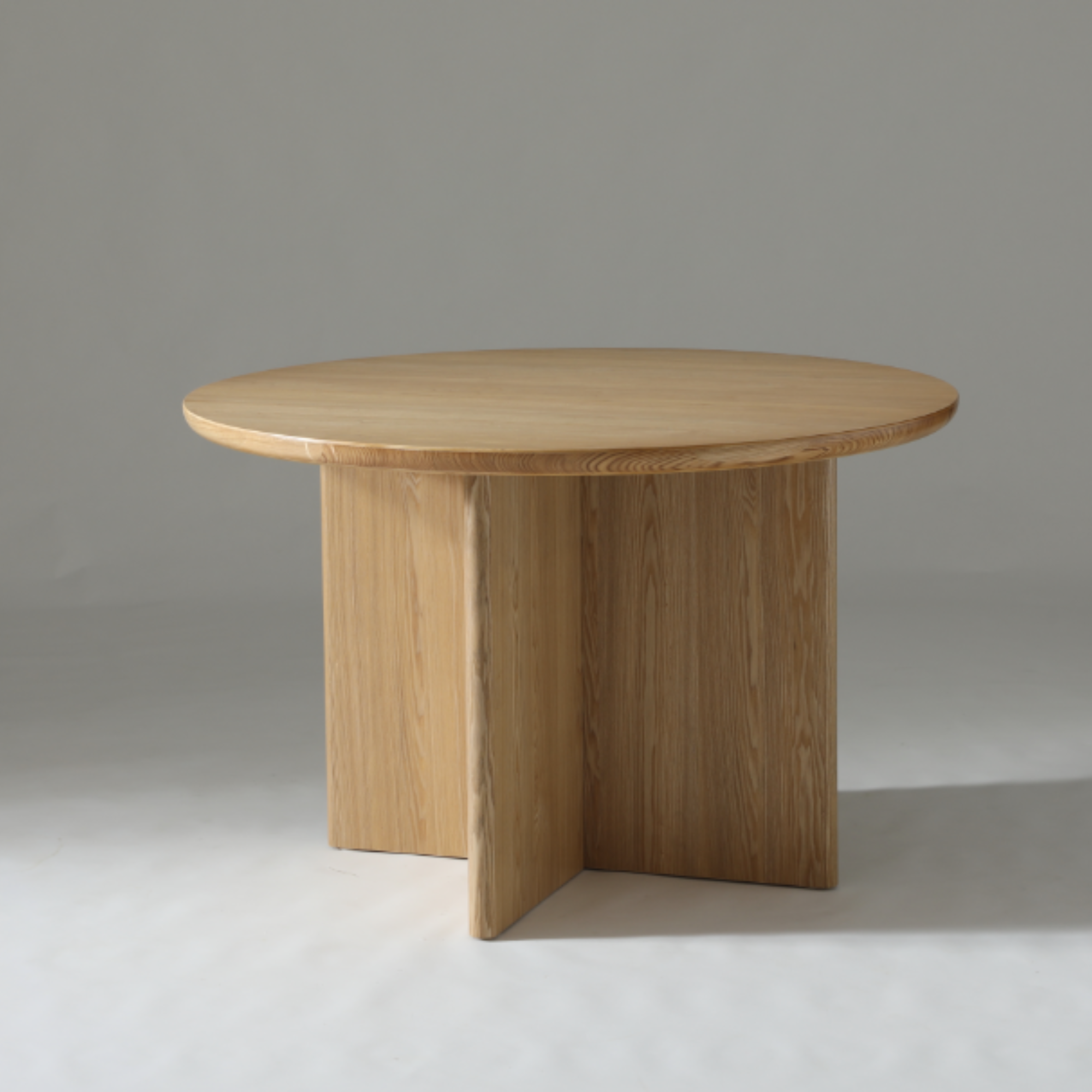 Natural Ash round dining table with subtle wood grain and light, modern coastal style.