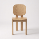 A minimalist light oak wood chair with a rounded rectangular backrest, a gently curved seat, and four straight legs, shown against a plain white studio background.