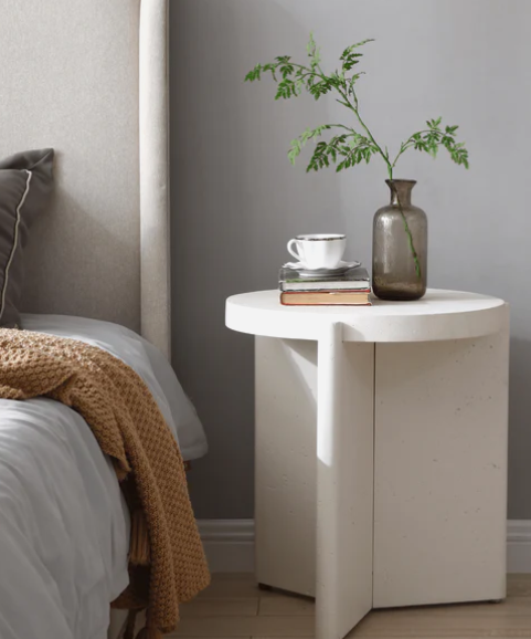 Modern white round coffee table, 80 cm diameter, airy coastal living room with oak floor, rattan tray, ceramic vase, natural light.